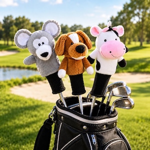 Op de afbeelding: Drie pluche golfclub headcovers in de vorm van dieren, waaronder een grijze muis, een bruin-witte hond en een zwart-witte koe met een roze snuit. Elke hoes heeft een lange zwarte gebreide sok als basis en zit vast aan een metalen golfclubschacht.