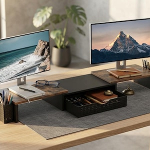 May include: A modular desk organizer set featuring two wood-grain monitor stands, a central black drawer unit, and two black perforated metal pen holders. The setup supports two computer monitors displaying mountain and ocean landscapes.