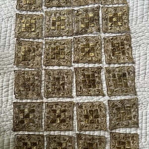 May include: Twenty-four square-shaped fabric patches with gold embroidery on a white background.