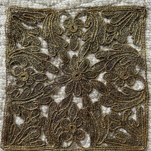 Peut inclure: Un carré de tissu avec un motif brodé en or de fleurs et de feuilles stylisées.