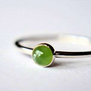 Op de afbeelding: Een zilveren ring met een groene edelsteen in het midden.