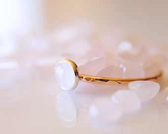 Könnte beinhalten: Ein zarter Goldring mit einem runden, hellrosa Edelstein. Der Ring ist von kleinen, hellrosa Steinen umgeben.