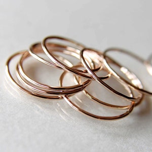 May include: A set of thin, rose gold stacking rings. The rings are made of a smooth, hammered metal and are arranged in a loose pile.