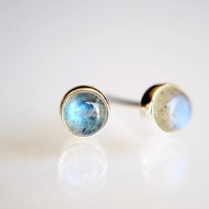 May include: A pair of silver stud earrings with round, iridescent moonstone gemstones.