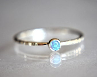 May include: A delicate silver ring with a small, round, light blue opal gemstone.