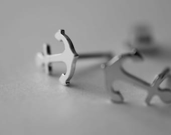 Könnte beinhalten: Ein Paar silberne Ankerohrringe. Die Ohrringe sind klein und zart und wären ein tolles Geschenk für jemanden, der das Meer liebt.