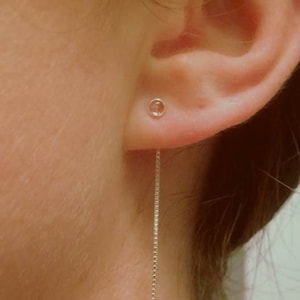 May include: A silver chain earring with a small round charm hanging from the bottom. The earring is worn in the left ear of a person.
