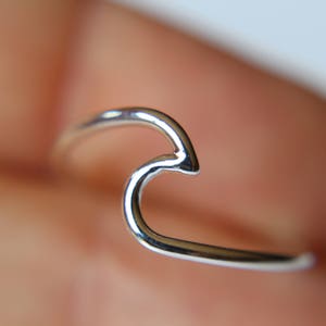 May include: A silver wave ring. The ring is made of a thin, smooth metal and is shaped like a wave.