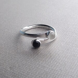 May include: A silver ring with a white and black stone. The ring is twisted and has a unique design.