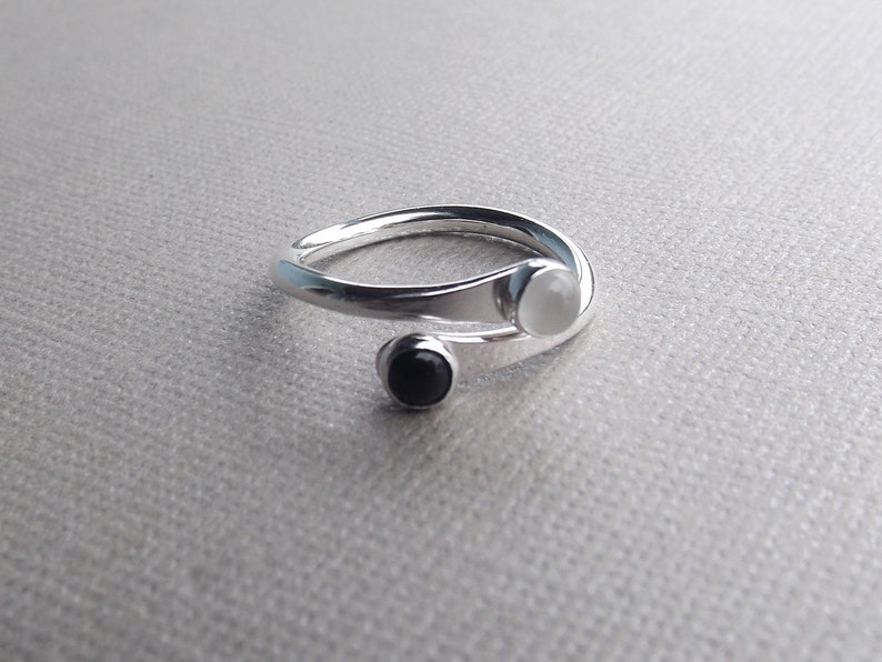 May include: A silver ring with a white and black stone. The ring is twisted and has a unique design.