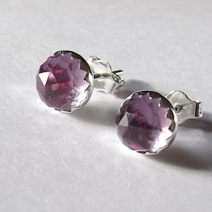 Peut inclure: Une paire de boucles d'oreilles en argent avec une pierre pr&eacute;cieuse violette dans chacune. Les pierres pr&eacute;cieuses sont facett&eacute;es et ont une forme ronde.