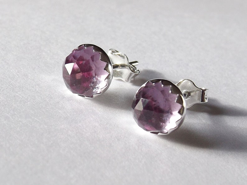 Peut inclure: Une paire de boucles d'oreilles en argent avec une pierre pr&eacute;cieuse violette dans chacune. Les pierres pr&eacute;cieuses sont facett&eacute;es et ont une forme ronde.
