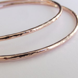 May include: Two hammered rose gold bangle bracelets. The bracelets are stacked on top of each other.