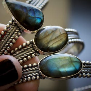 May include: Three silver cuff bracelets featuring labradorite gemstones. Each bracelet has a textured band with beaded and twisted wire details. The stones are set in smooth bezels, displaying iridescent blue and gold flashes.