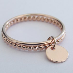 May include: A delicate rose gold ring with a beaded band and a small, round charm hanging from it.