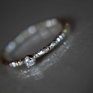 Puede incluir: Un delicado anillo de plata con un peque&ntilde;o diamante transparente engastado en el centro. La banda est&aacute; texturizada con peque&ntilde;as cuentas.