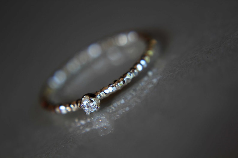 Puede incluir: Un delicado anillo de plata con un peque&ntilde;o diamante transparente engastado en el centro. La banda est&aacute; texturizada con peque&ntilde;as cuentas.