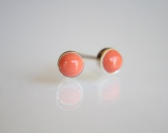 May include: A pair of silver stud earrings with round, coral-colored stones.