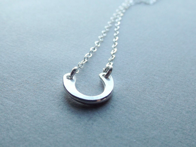 May include: A silver horseshoe pendant necklace. The horseshoe is a simple design with a smooth, polished finish.