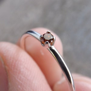 May include: A silver ring with a small, round, brown gemstone set in a prong setting.