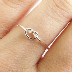 May include: A silver knot ring with a simple design. The ring is worn on a finger.