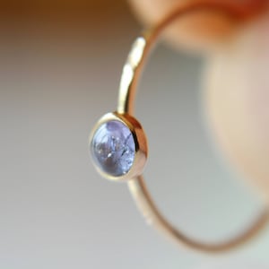 Puede incluir: Un delicado anillo de oro con una sola piedra preciosa redonda de color p&uacute;rpura claro engastada en el centro.