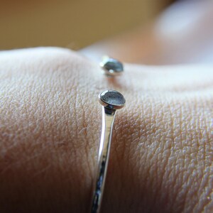 May include: A silver bangle bracelet with two round, light blue gemstones. The bracelet is on a person's wrist.