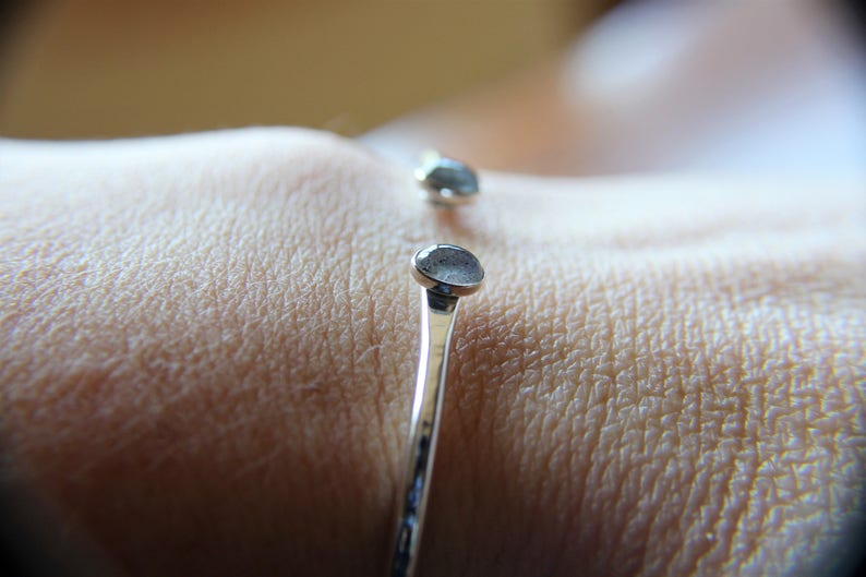 May include: A silver bangle bracelet with two round, light blue gemstones. The bracelet is on a person's wrist.
