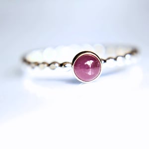 Puede incluir: Un anillo de plata con una piedra preciosa redonda de color rosa engastada en el centro. La banda del anillo est&aacute; texturizada con peque&ntilde;as cuentas.
