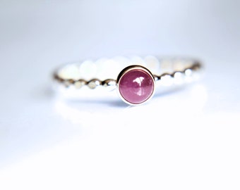 May include: A silver ring with a round, pink gemstone set in the center. The ring band is textured with small beads.