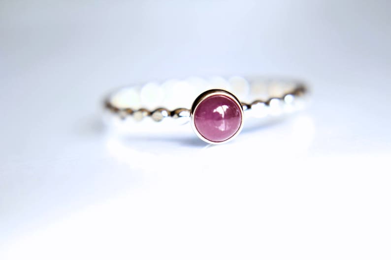 Puede incluir: Un anillo de plata con una piedra preciosa redonda de color rosa engastada en el centro. La banda del anillo est&aacute; texturizada con peque&ntilde;as cuentas.