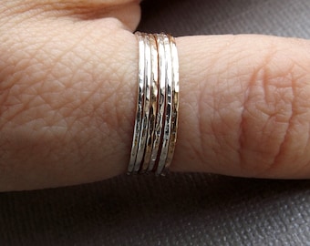 May include: A stack of five thin, hammered metal rings in silver and gold tones. The rings are worn on a finger.