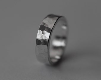 May include: A silver hammered band ring. The ring is made of a smooth, polished metal and has a textured, hammered finish.