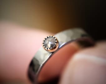 May include: A silver band ring with a hammered finish and a single gray diamond set in a rose gold bezel.