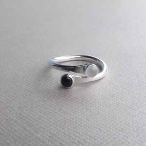 May include: A silver ring with a white and black stone set in the band. The ring is twisted and the stones are set on the top of the band.