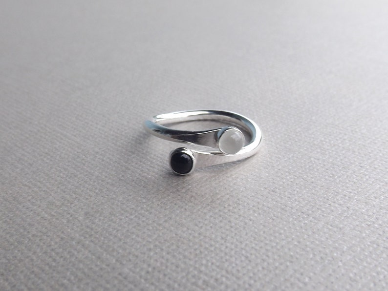 May include: A silver ring with a white and black stone set in the band. The ring is twisted and the stones are set on the top of the band.