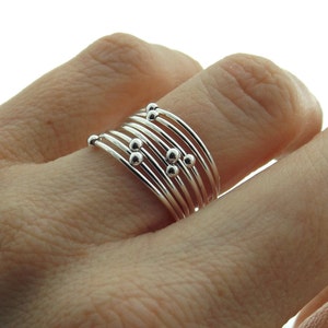 May include: A silver ring with multiple bands and small silver beads. The ring is worn on a finger.