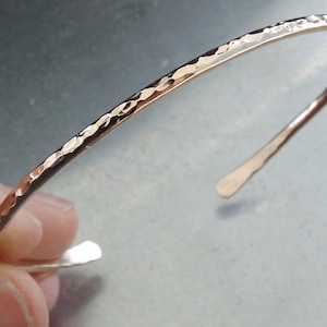 May include: A hammered gold bangle bracelet with a simple, open design.