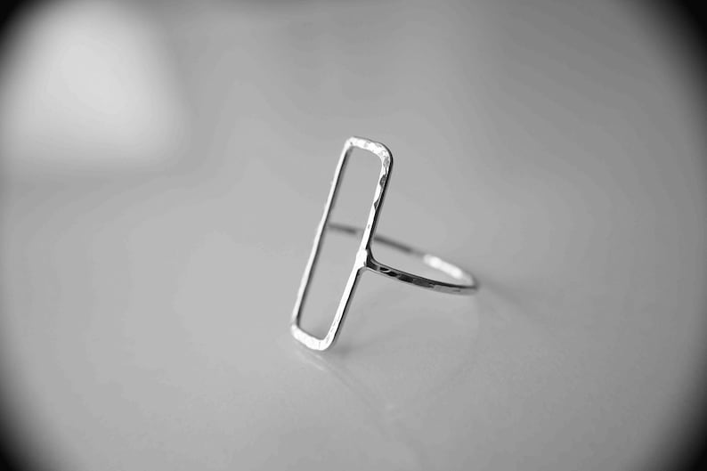 May include: A silver ring with a hammered finish, featuring a rectangular open design.