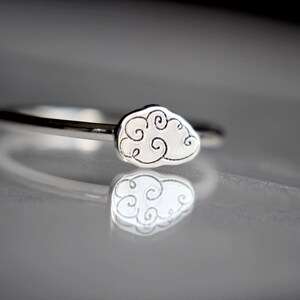 Puede incluir: Un anillo de plata con un diseño de nube. La nube está hecha de remolinos y está elevada de la banda del anillo.