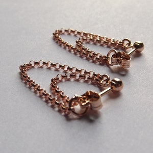May include: A pair of rose gold chain earrings with a small ball at the end of each chain.