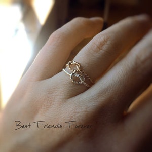 May include: Two gold rings intertwined in a knot design. The rings are worn on a finger and the caption "Best Friends Forever" is visible below.