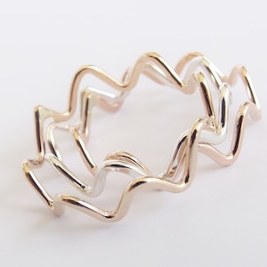 May include: Three interlocking rings made of silver and rose gold. The rings are wavy and have a zig-zag pattern.