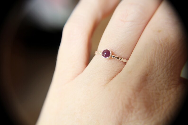 Puede incluir: Un anillo de plata con una peque&ntilde;a piedra preciosa redonda de color p&uacute;rpura engastada en el centro. El anillo est&aacute; hecho de peque&ntilde;as cuentas.