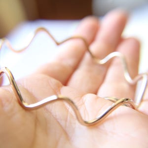 May include: A gold-toned wavy metal bracelet. The bracelet is made of a thin, flexible metal and has a unique, organic shape.
