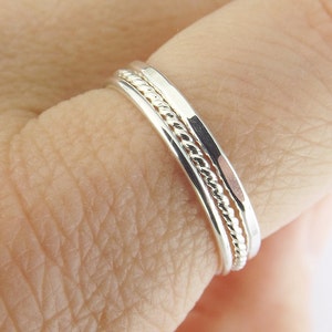 K&ouml;nnte beinhalten: Drei &uuml;bereinander getragene Silberringe, einer mit einem gedrehten Design, an einem Finger getragen.
