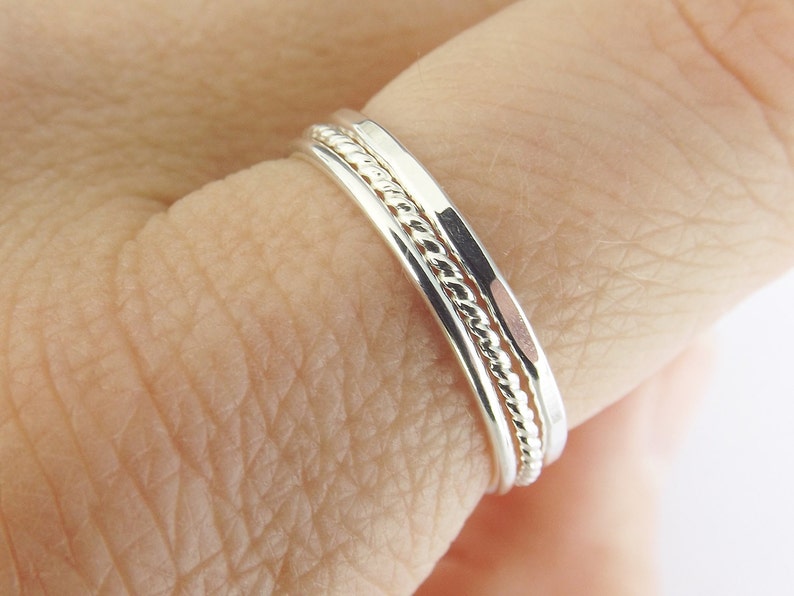 K&ouml;nnte beinhalten: Drei &uuml;bereinander getragene Silberringe, einer mit einem gedrehten Design, an einem Finger getragen.