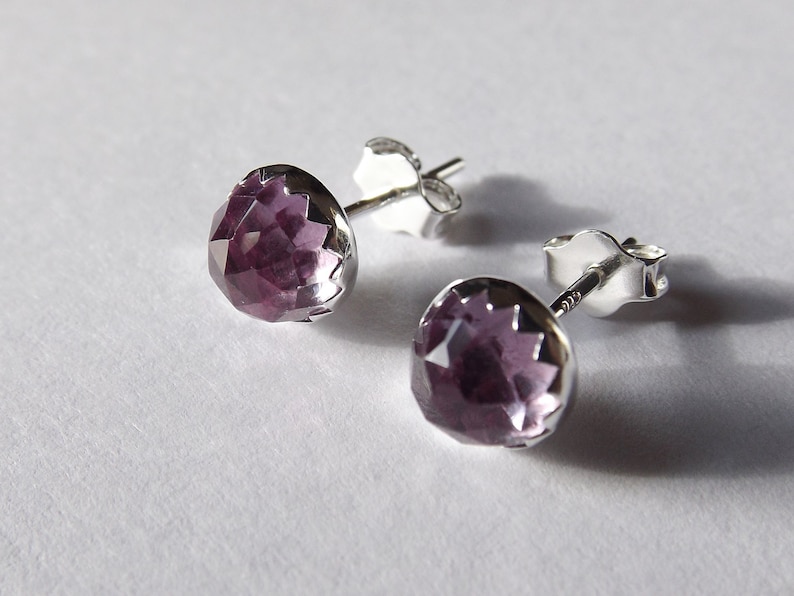 Peut inclure: Une paire de boucles d'oreilles en argent avec une pierre pr&eacute;cieuse violette au centre de chaque boucle d'oreille.
