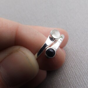 May include: A silver ring with two round stones, one white and one black.