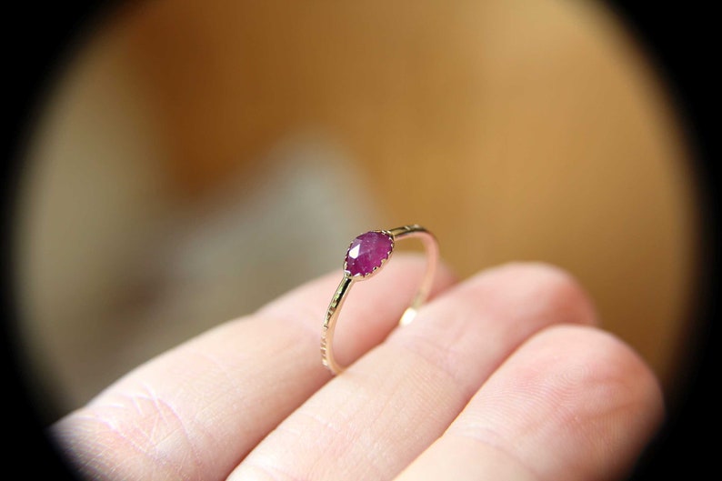 May include: A delicate gold ring with a single, faceted, pink gemstone set in the center.